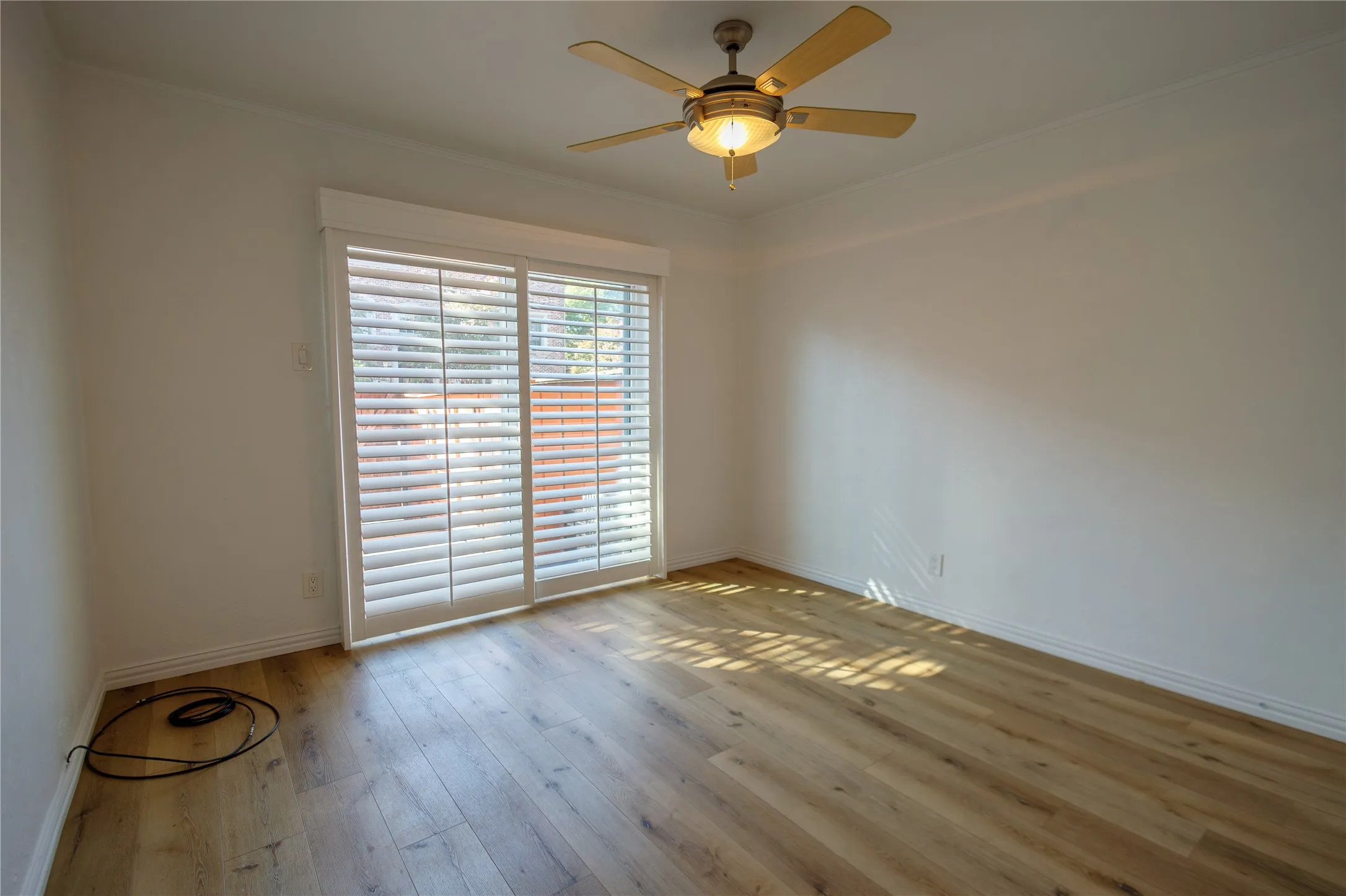 Wood-finish flooring, white walls, and a ceiling fan with integrated lighting