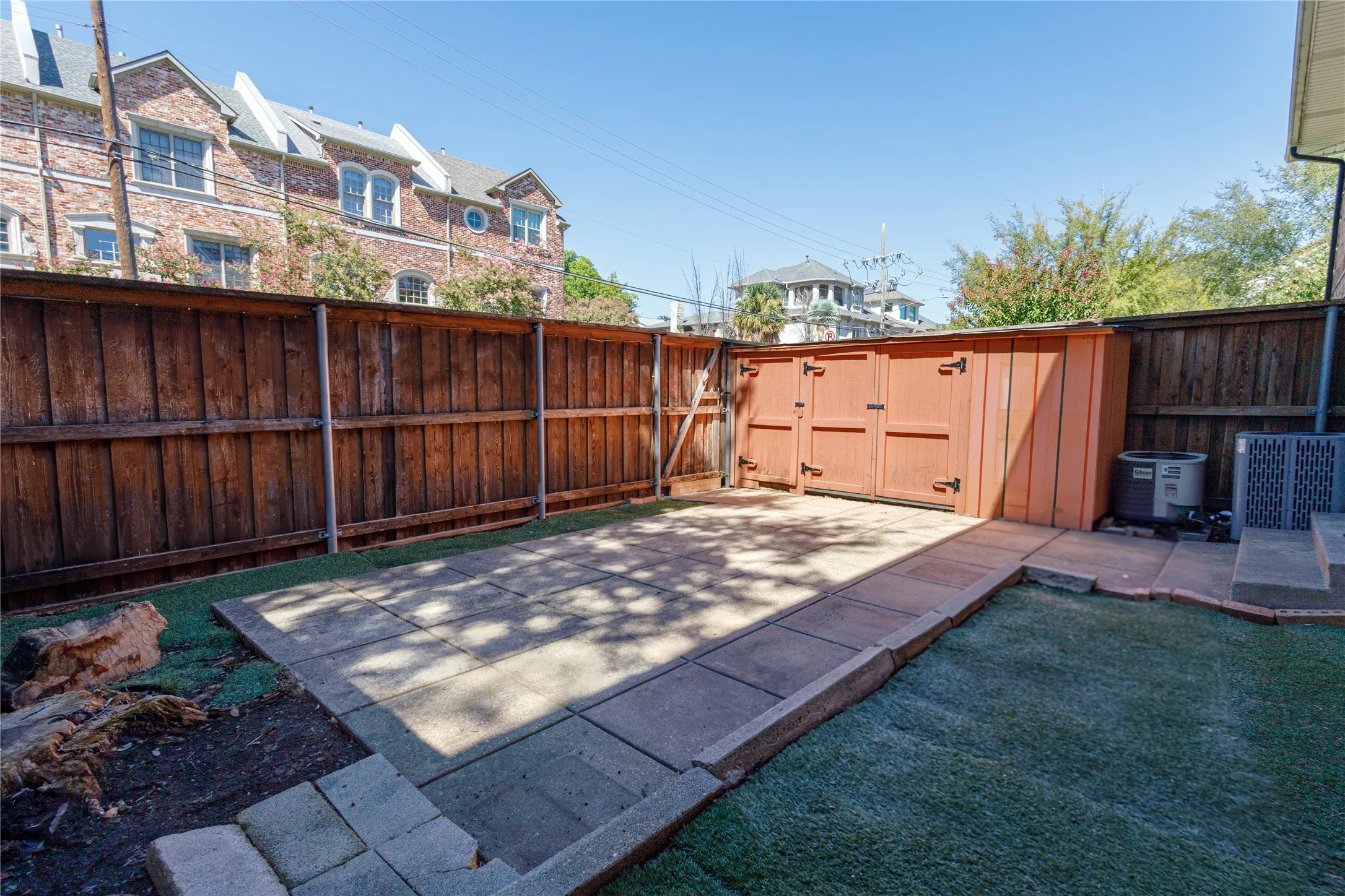 Fenced backyard featuring a paver patio, artificial turf, and a storage shed