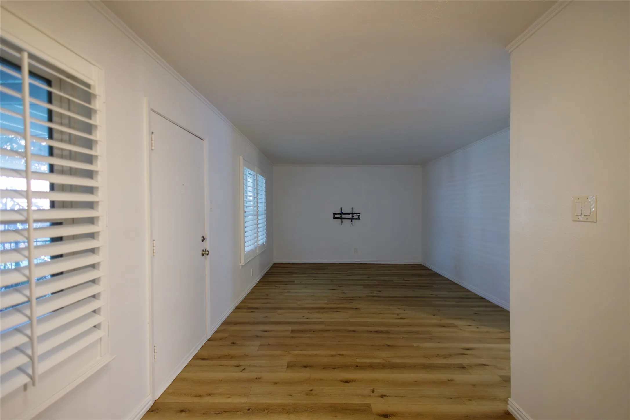 Wood-finish flooring, white plantation shutters, and a wall-mounted light switch