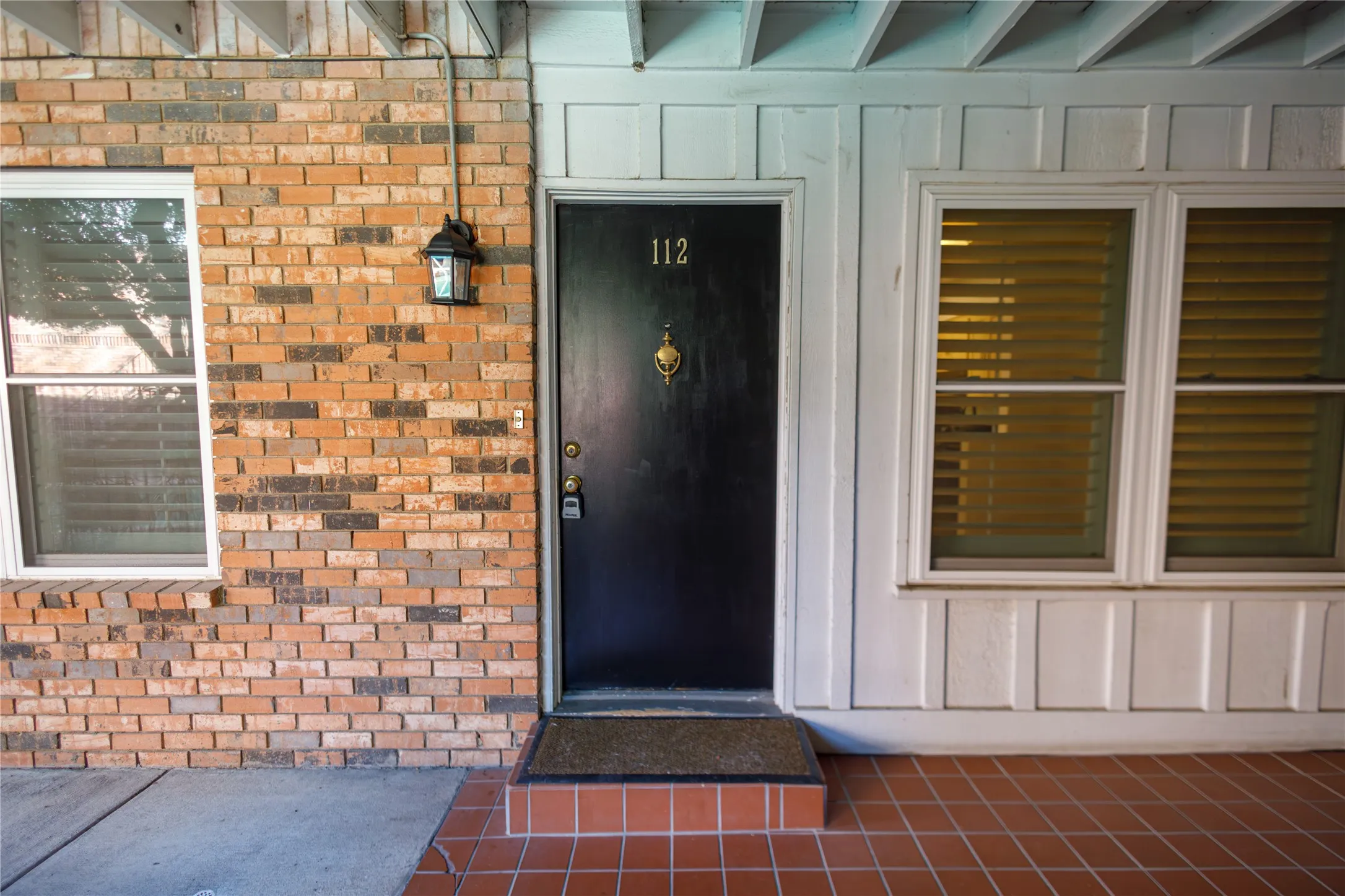 Brick exterior with an entryway sconce, a dark-finish entry door with a knocker, and white-framed windows