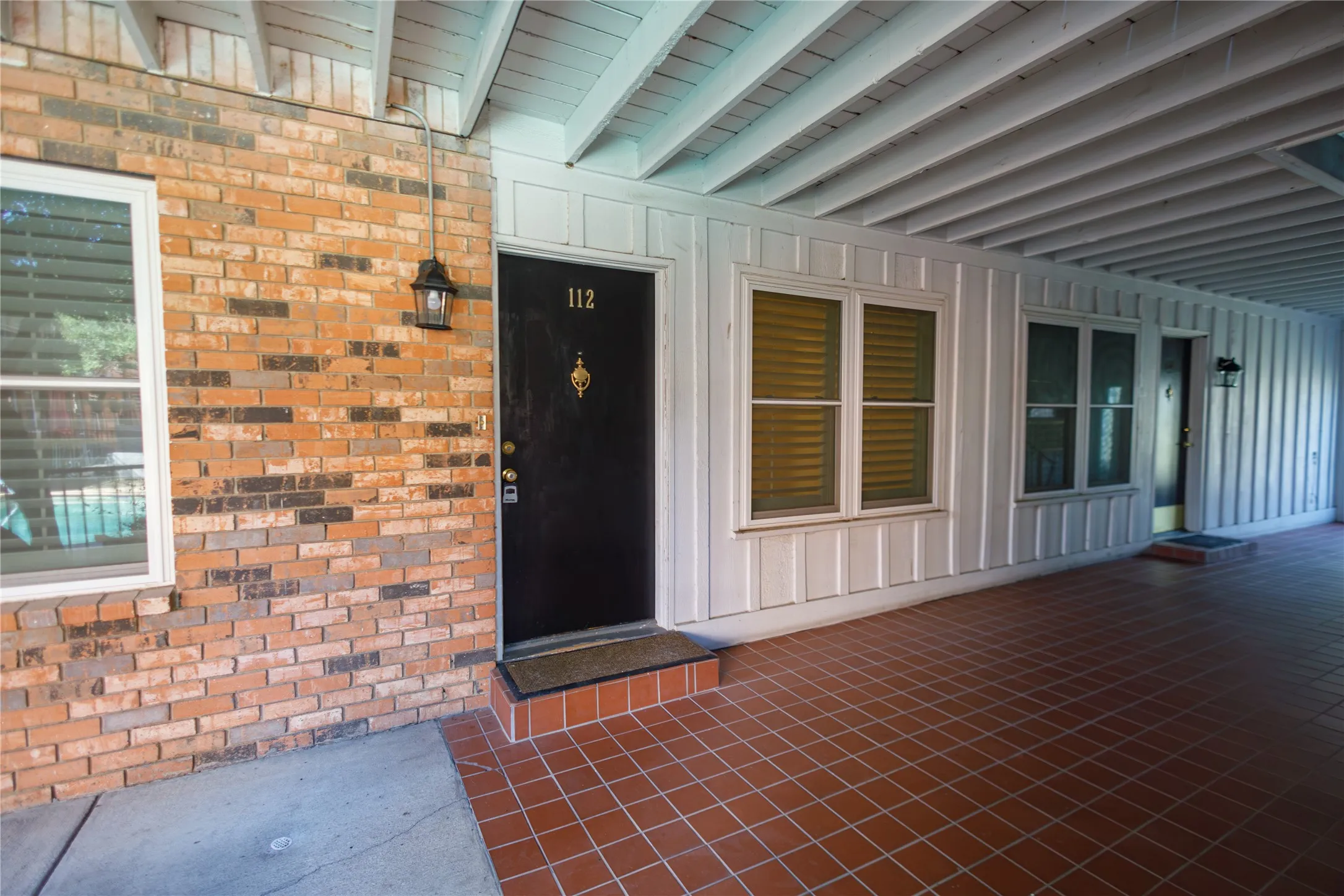 Brick exterior with a covered entry, white vertical panel siding, and a tile-finish floor