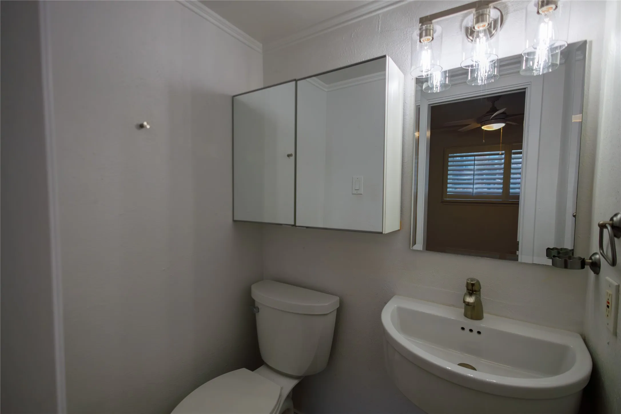 Wall-mounted sink with gold-tone faucet, mirrored medicine cabinet, and overhead vanity lighting