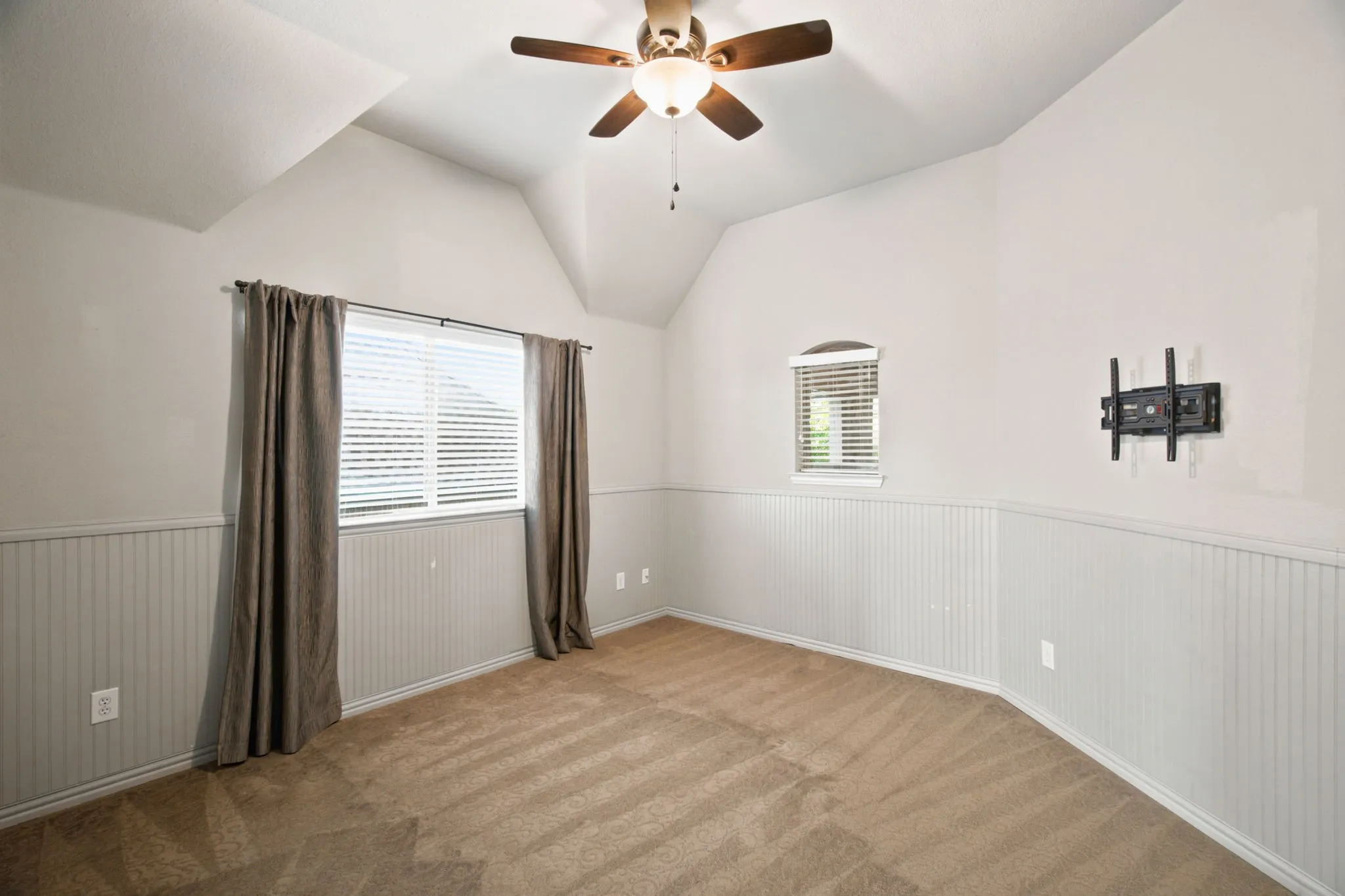 Vaulted ceiling with a ceiling fan light fixture, dual windows with blinds, and beadboard wainscoting