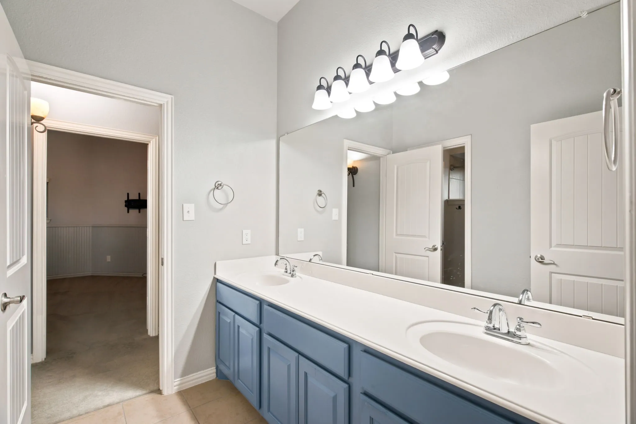 Dual vanity with white countertop and blue cabinetry, large wall-mounted mirror, and overhead lighting fixture