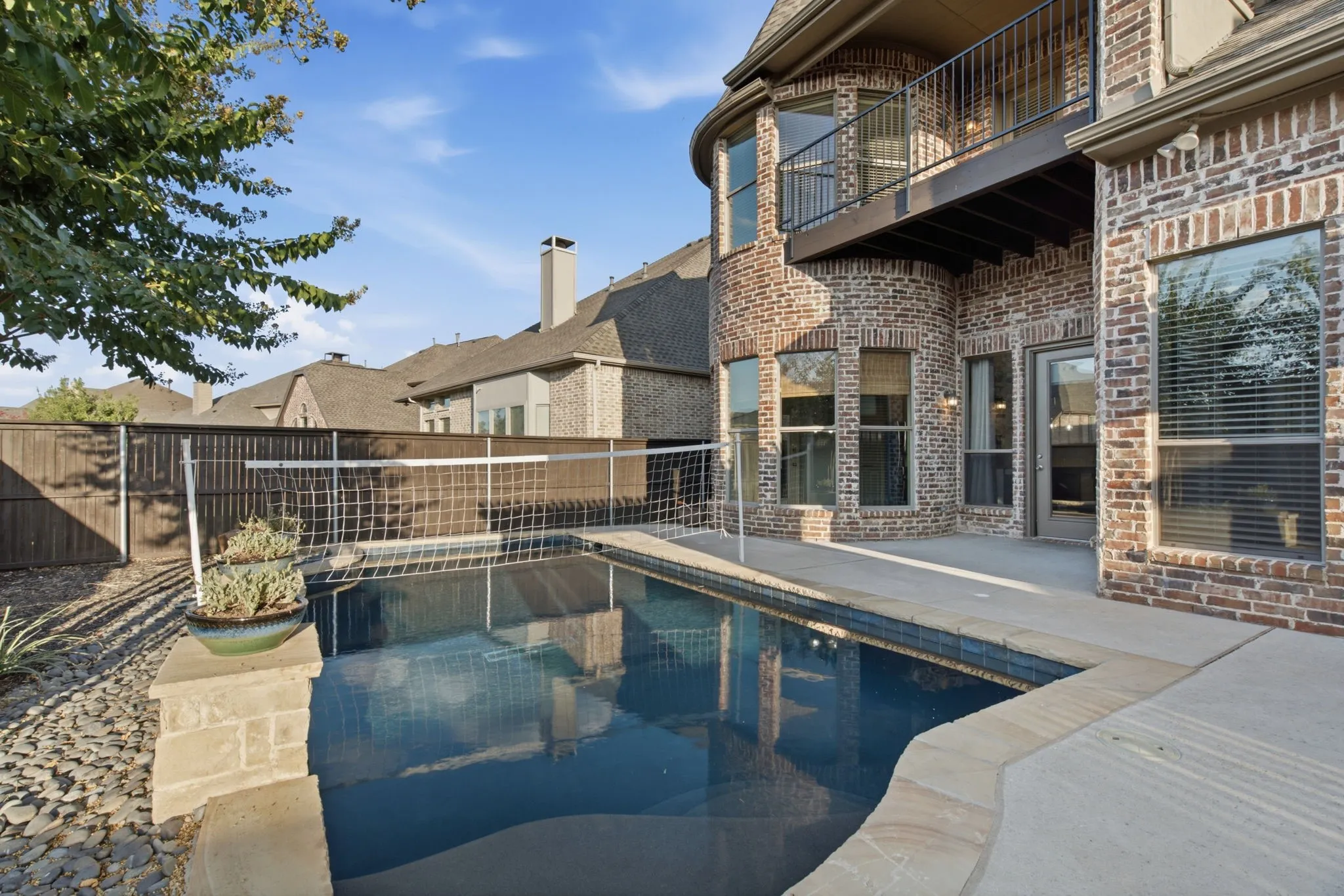 Brick exterior with multiple windows, a second-story balcony with metal railing, and a private pool