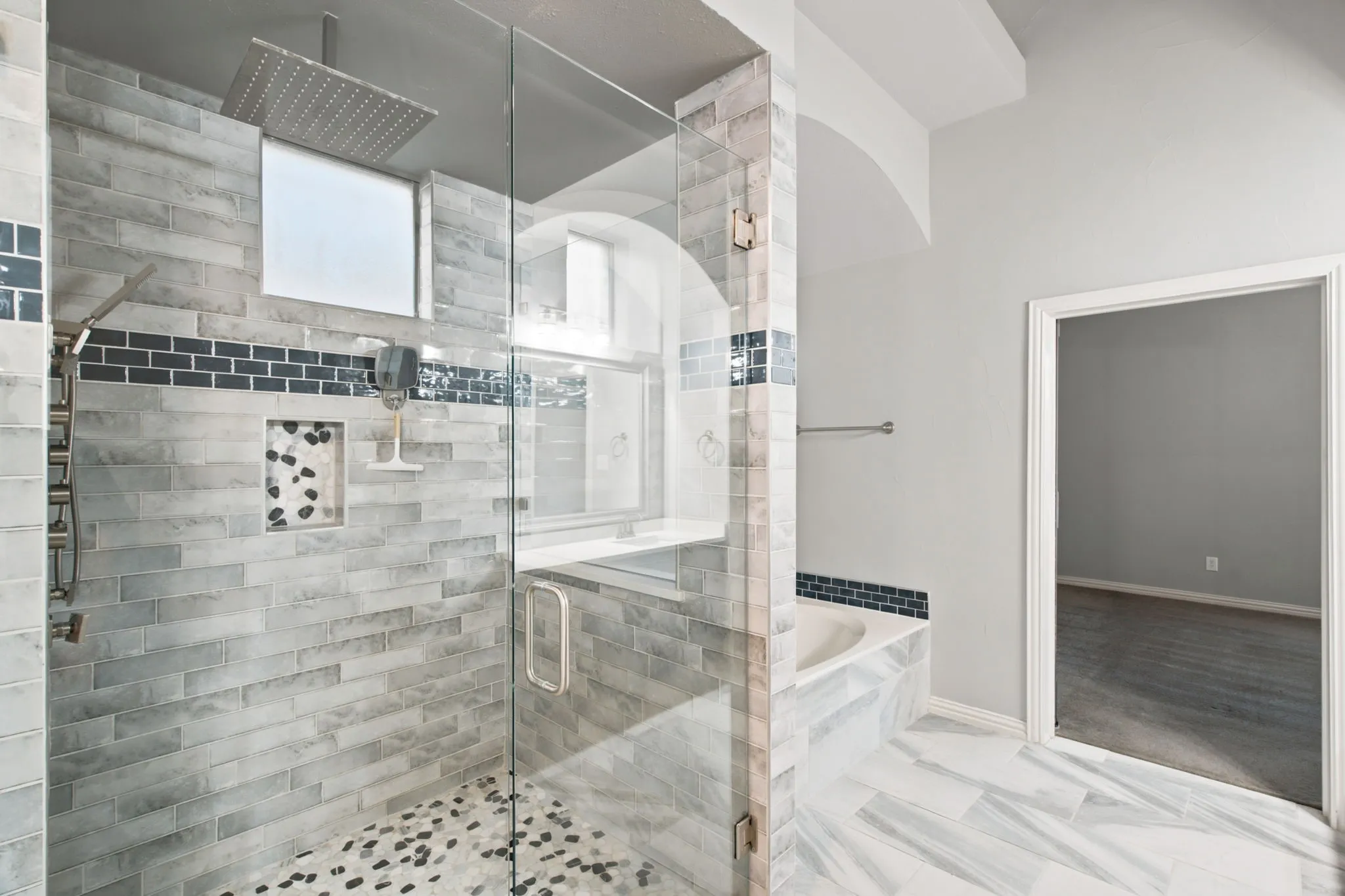 Spacious walk-in shower with glass enclosure, rain showerhead, mosaic tile accents, recessed shelf, and pebble-finish shower floor