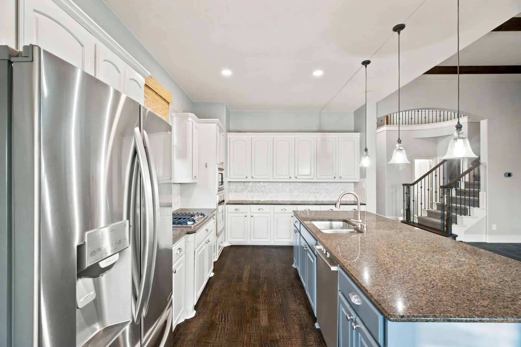 Kitchen featuring a stainless steel refrigerator, white cabinetry, a kitchen island with pendant lighting, a built-in sink, and wood-finish flooring