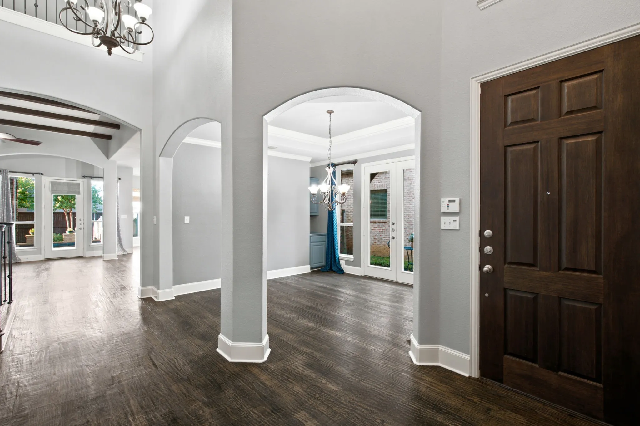Grand entry with dark wood-finish flooring, arched doorways, and a two-story ceiling featuring a chandelier