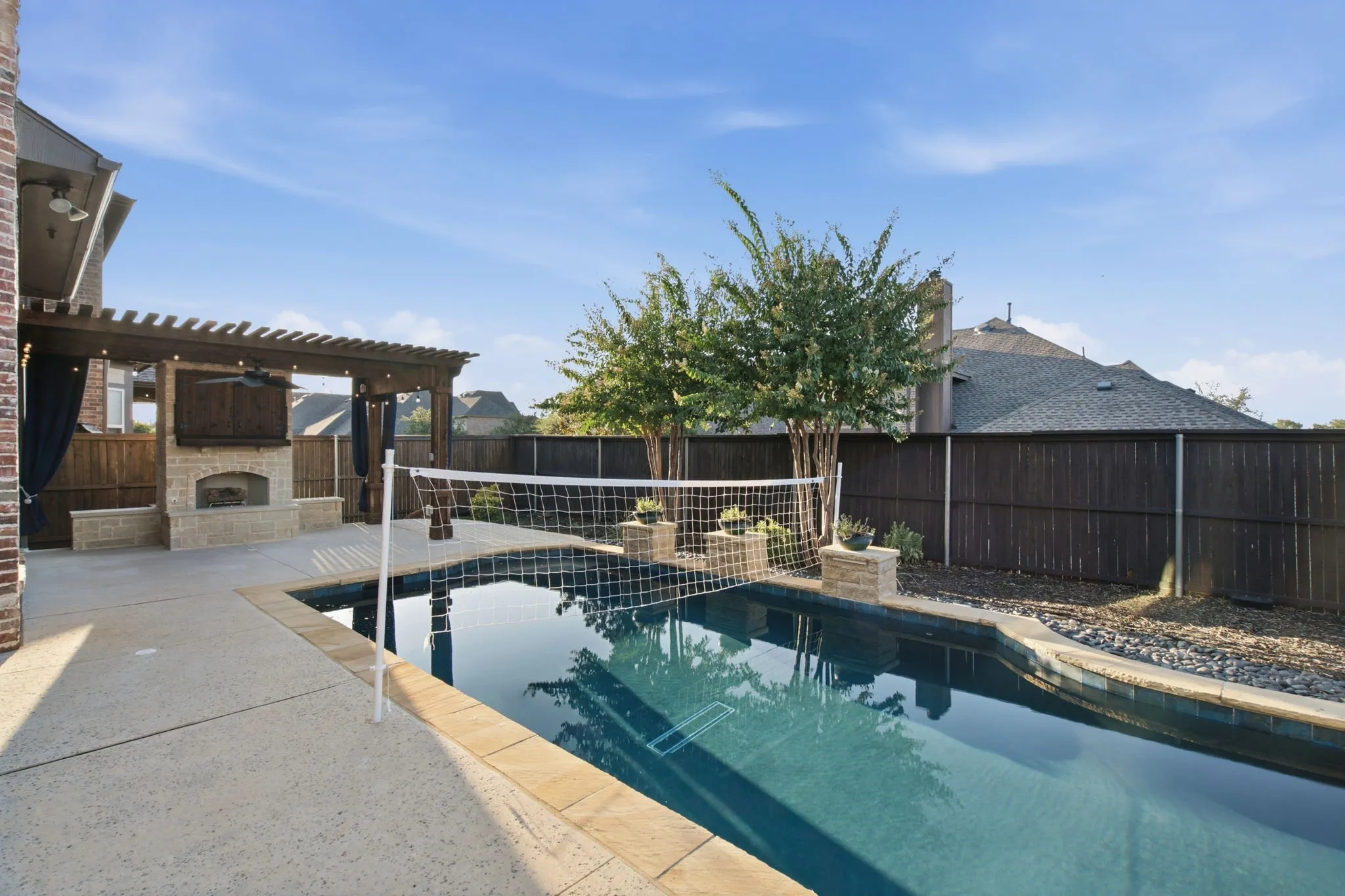 Swimming pool with stone coping, concrete patio, and pergola featuring a built-in outdoor fireplace