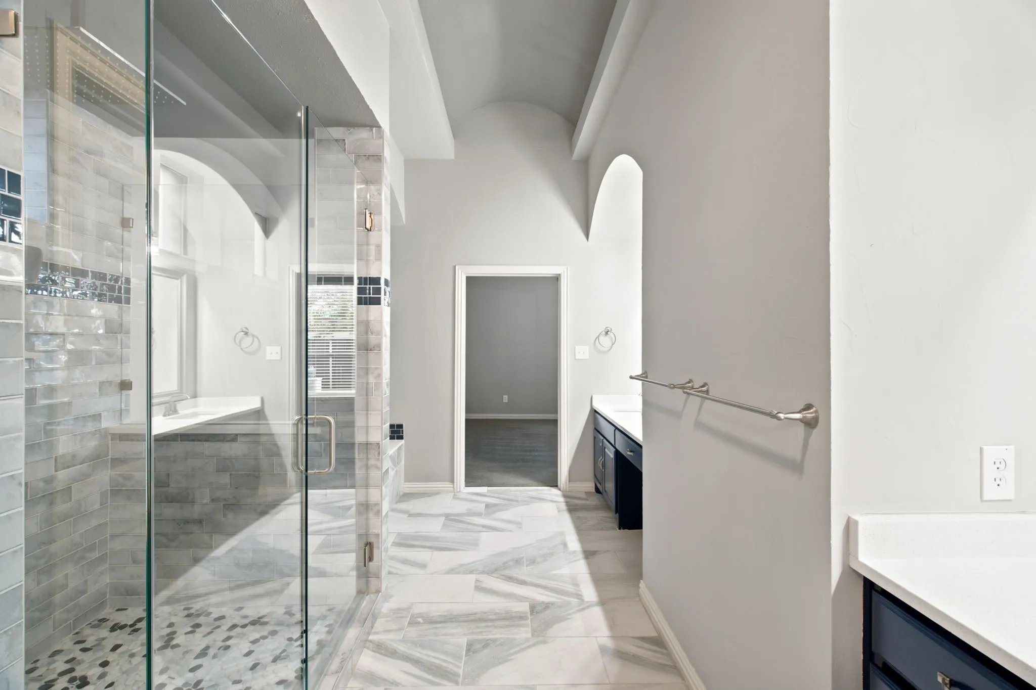 Glass-enclosed shower with pebble-finish flooring, tiled walls, and a decorative tile accent band