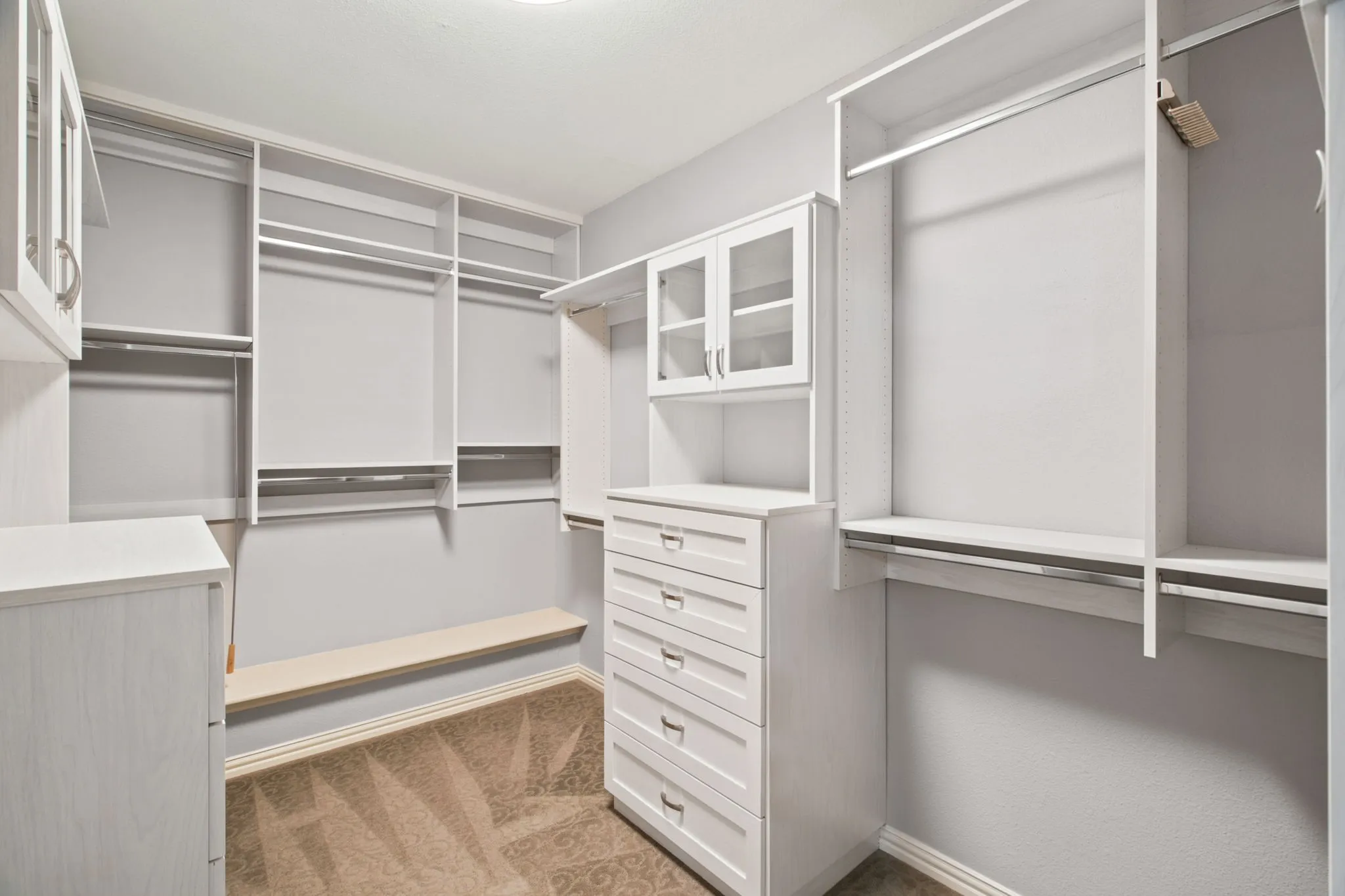 Custom closet system featuring multiple hanging rods, integrated shelving, built-in dresser with drawers, and glass-front upper cabinetry