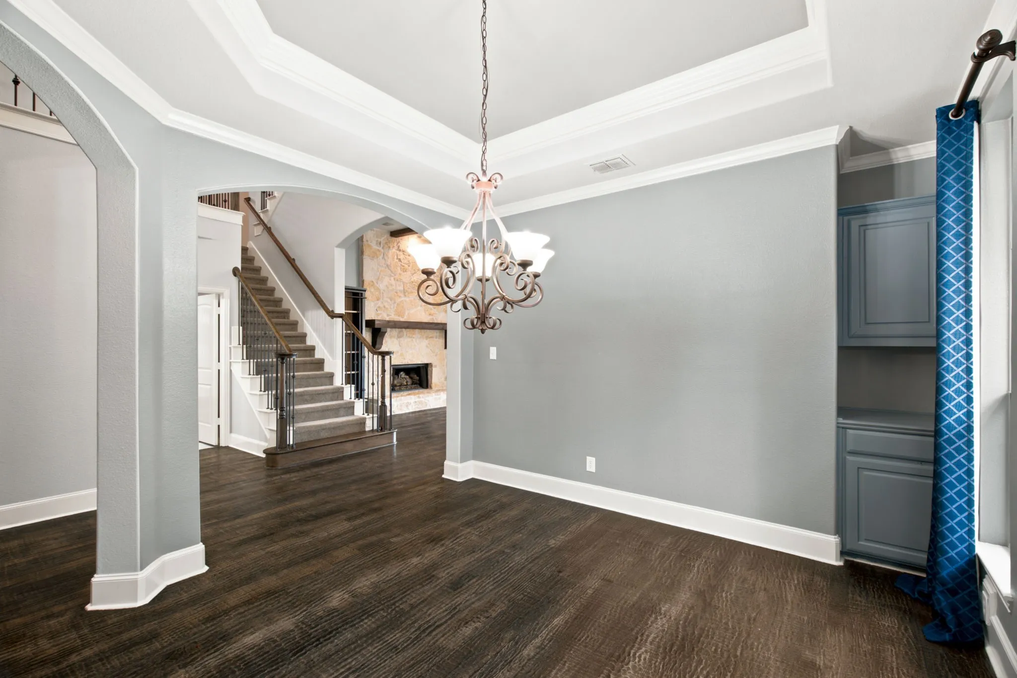 Tray ceiling with a decorative chandelier, wood-finish flooring, built-in cabinetry, arched doorways, and a staircase with an iron baluster