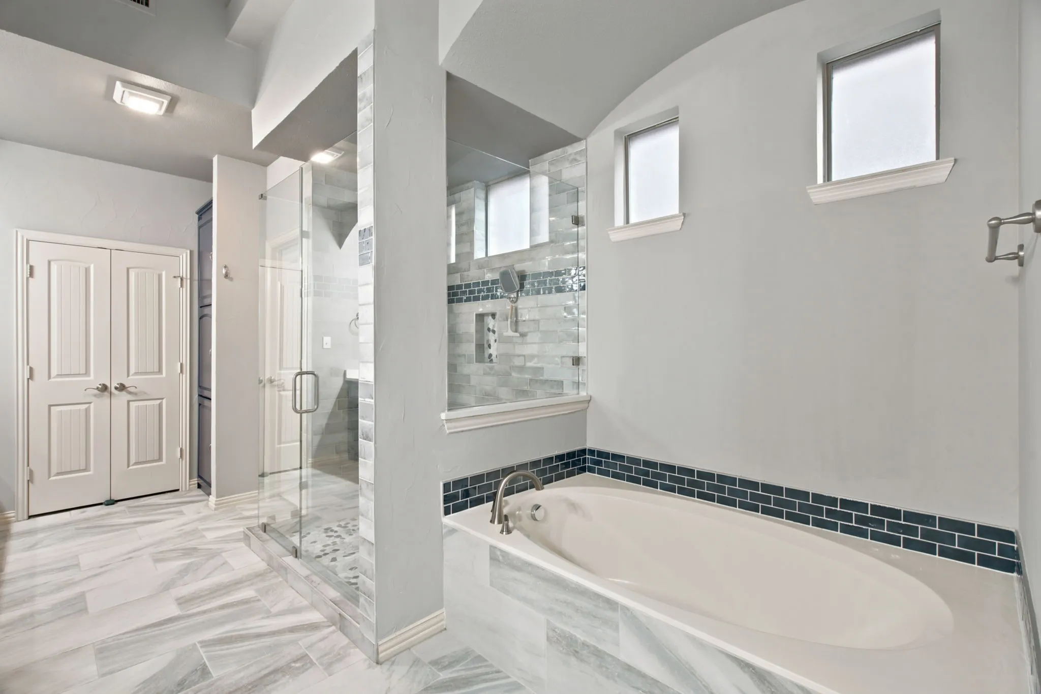 Walk-in shower with glass enclosure, soaking tub, and dual windows