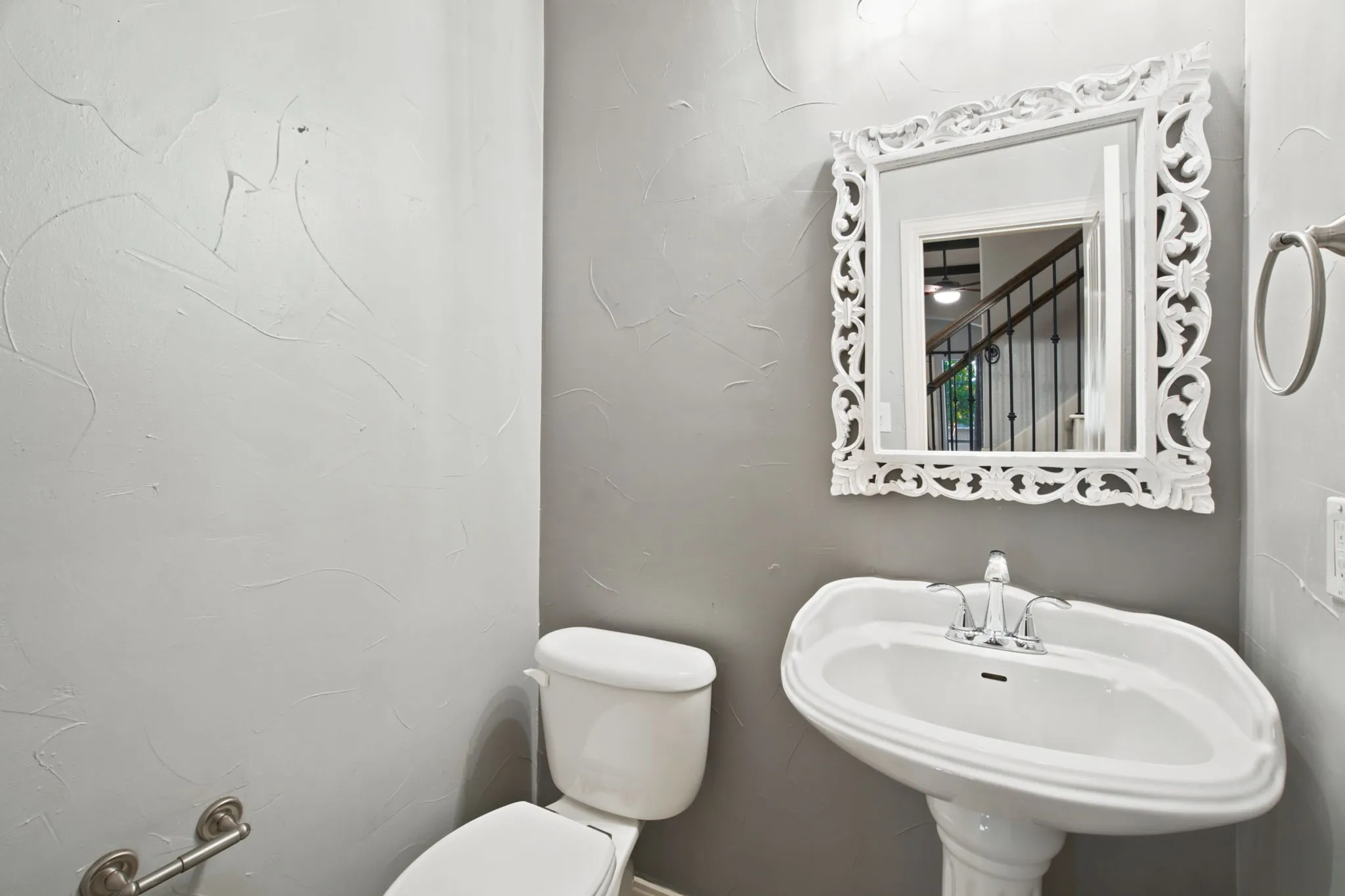 Pedestal sink with chrome fixtures, decorative framed mirror, and textured wall finish