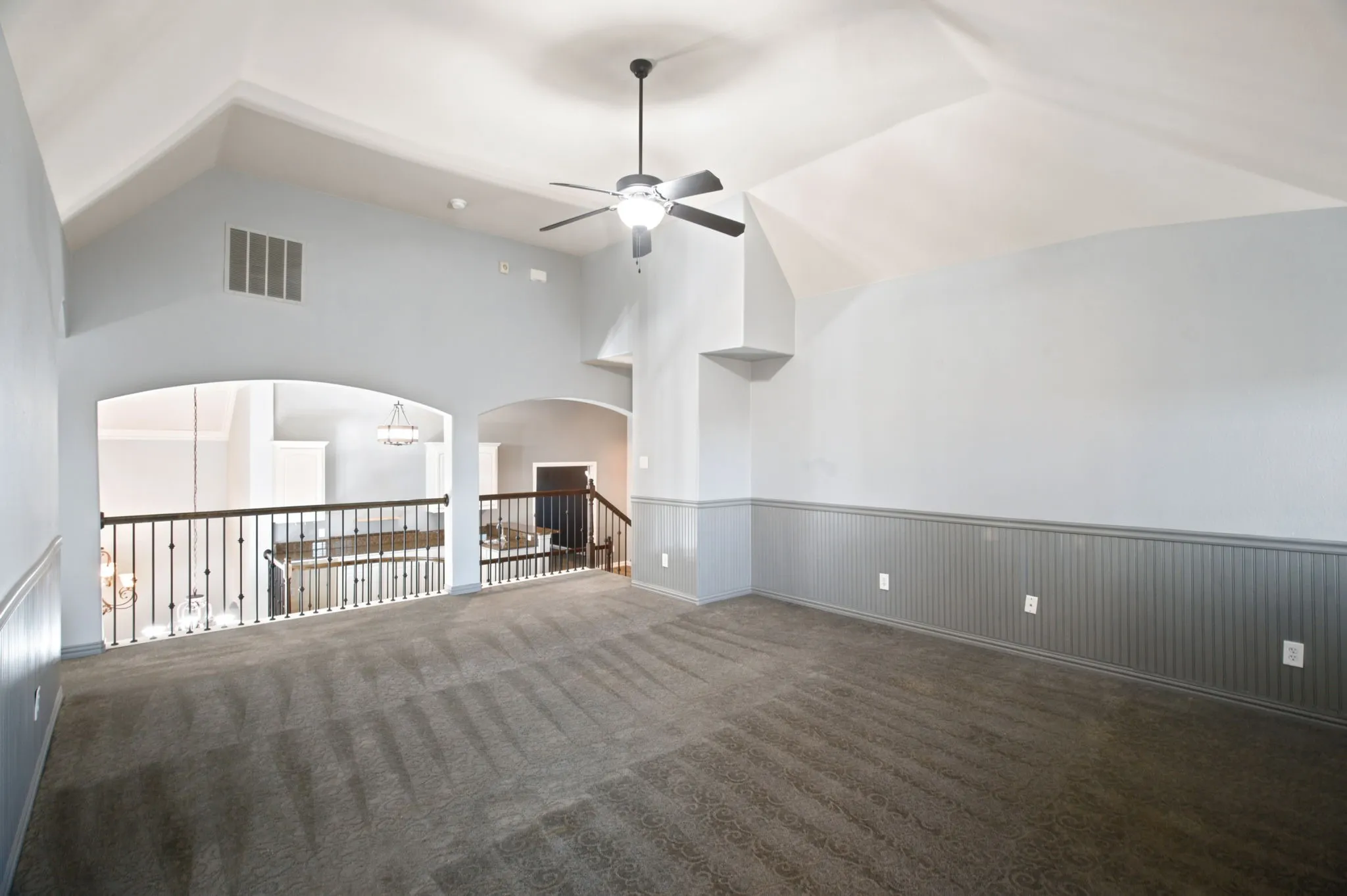Vaulted ceiling, ceiling fan, carpeted flooring, wainscoting, and arched openings