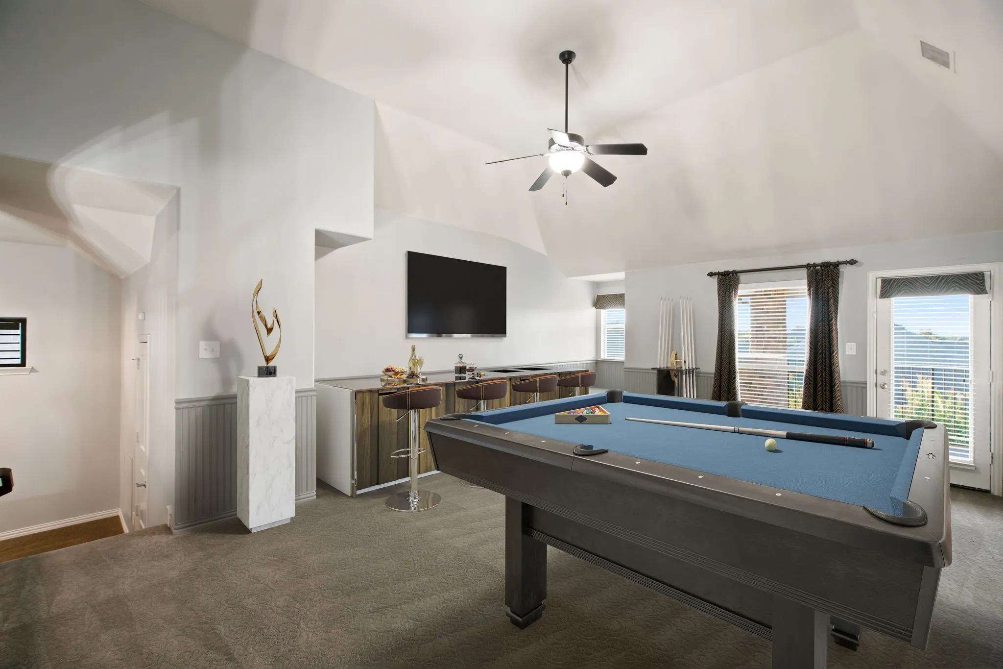 Vaulted ceiling with ceiling fan, built-in bar, wall-mounted television, and direct outdoor access.  Virtually staged