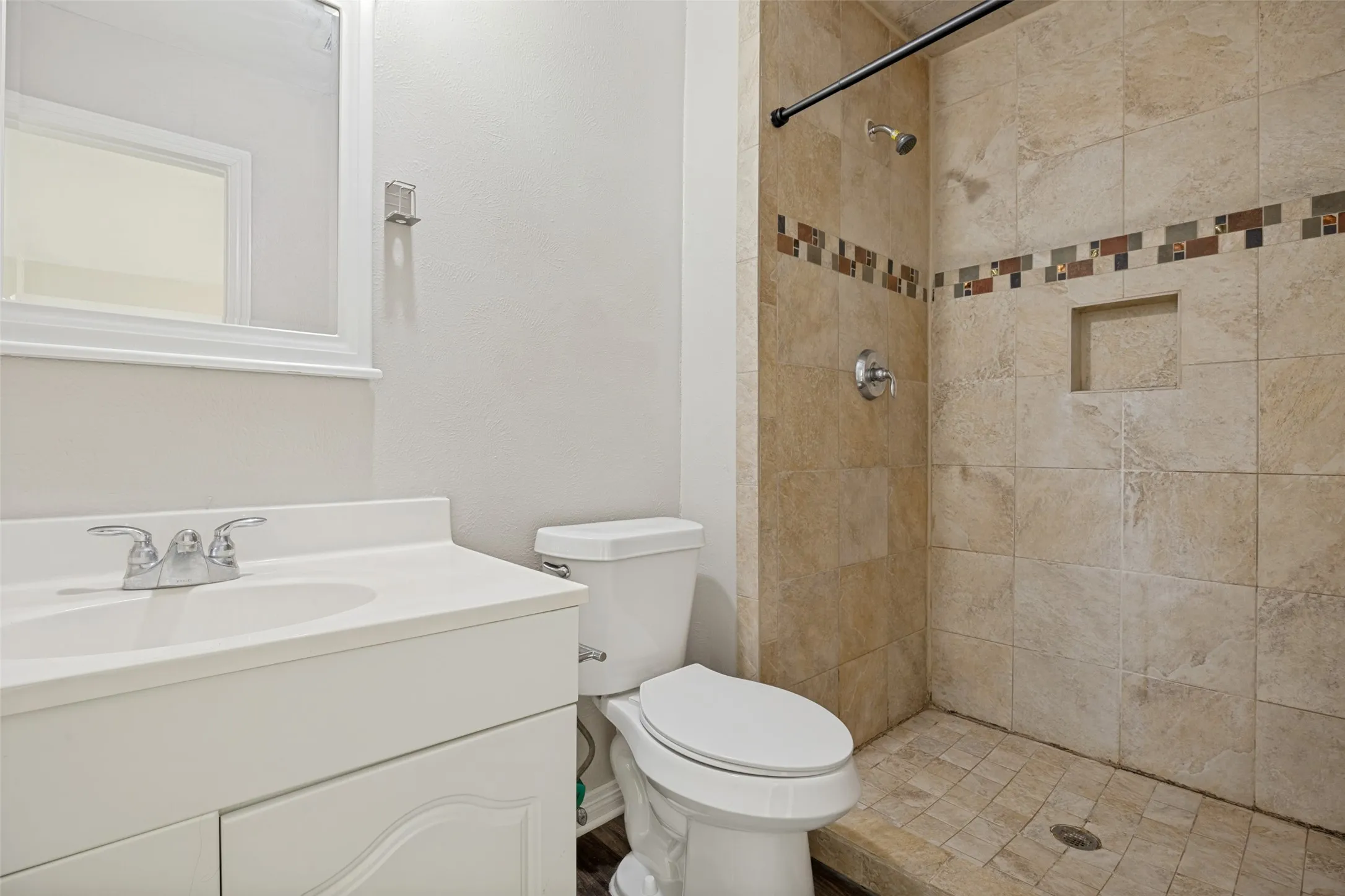 Primary shower with natural stone-look tile, decorative tile accent.