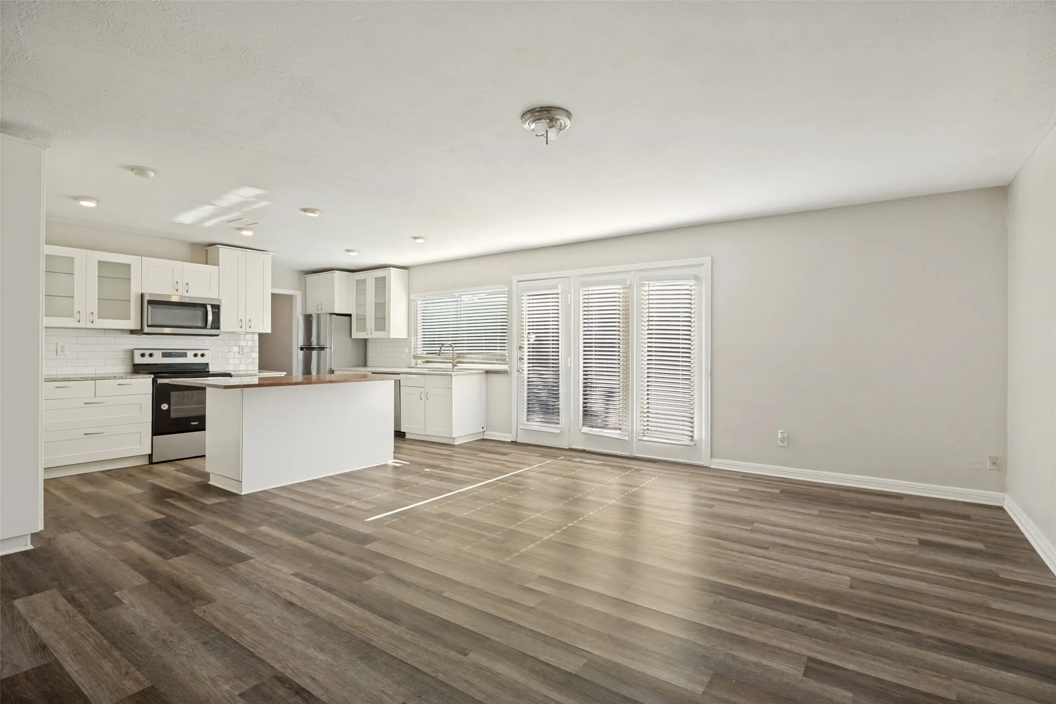 Open-concept living space featuring wood-finish flooring, white cabinetry, a kitchen island, stainless steel appliances, and double doors