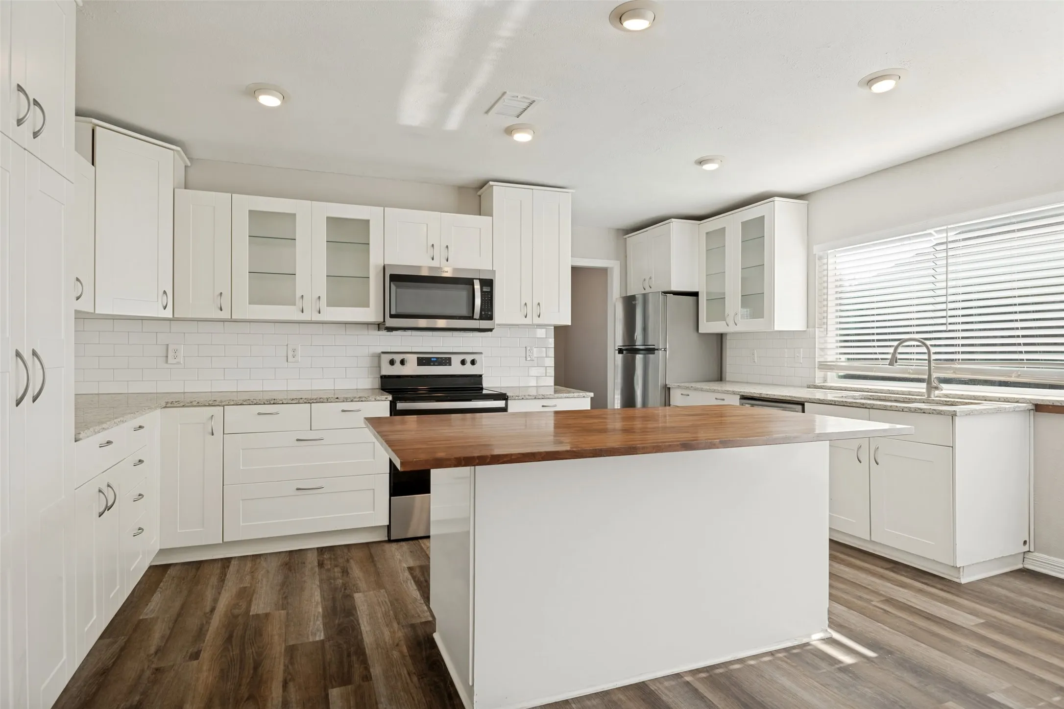 White cabinetry with stainless steel hardware, wood-finish flooring, recessed lighting, and a kitchen island with a wood countertop