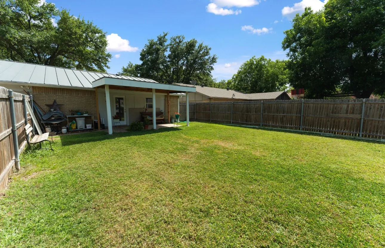 Expansive backyard featuring a manicured lawn, full perimeter fencing, and a covered patio area with a light-colored metal roof