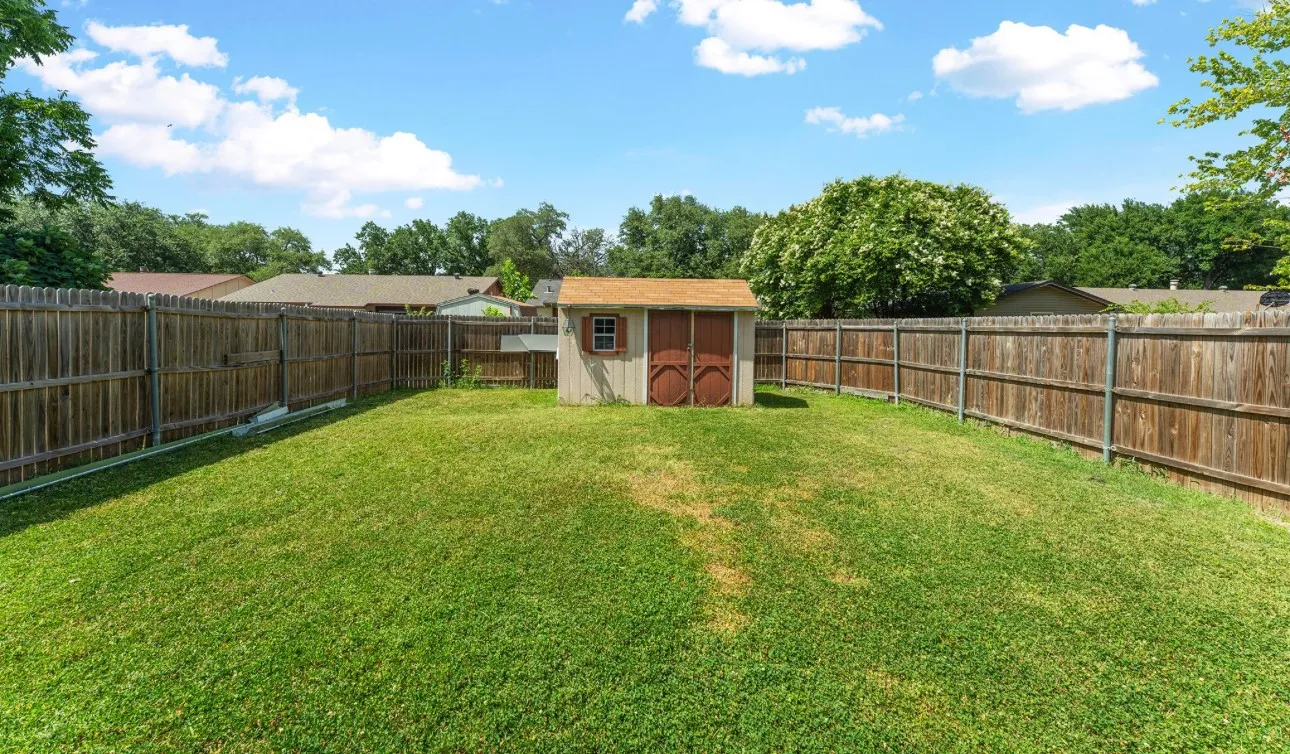 Expansive grassy yard with a wood privacy fence and a detached storage shed