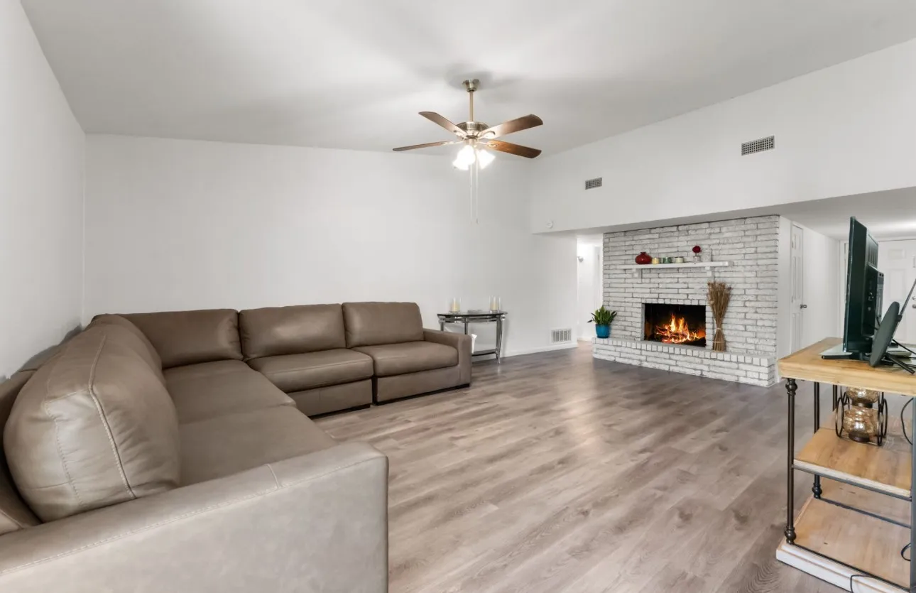 Living area with wood-finish flooring, a white brick fireplace, and a ceiling fan