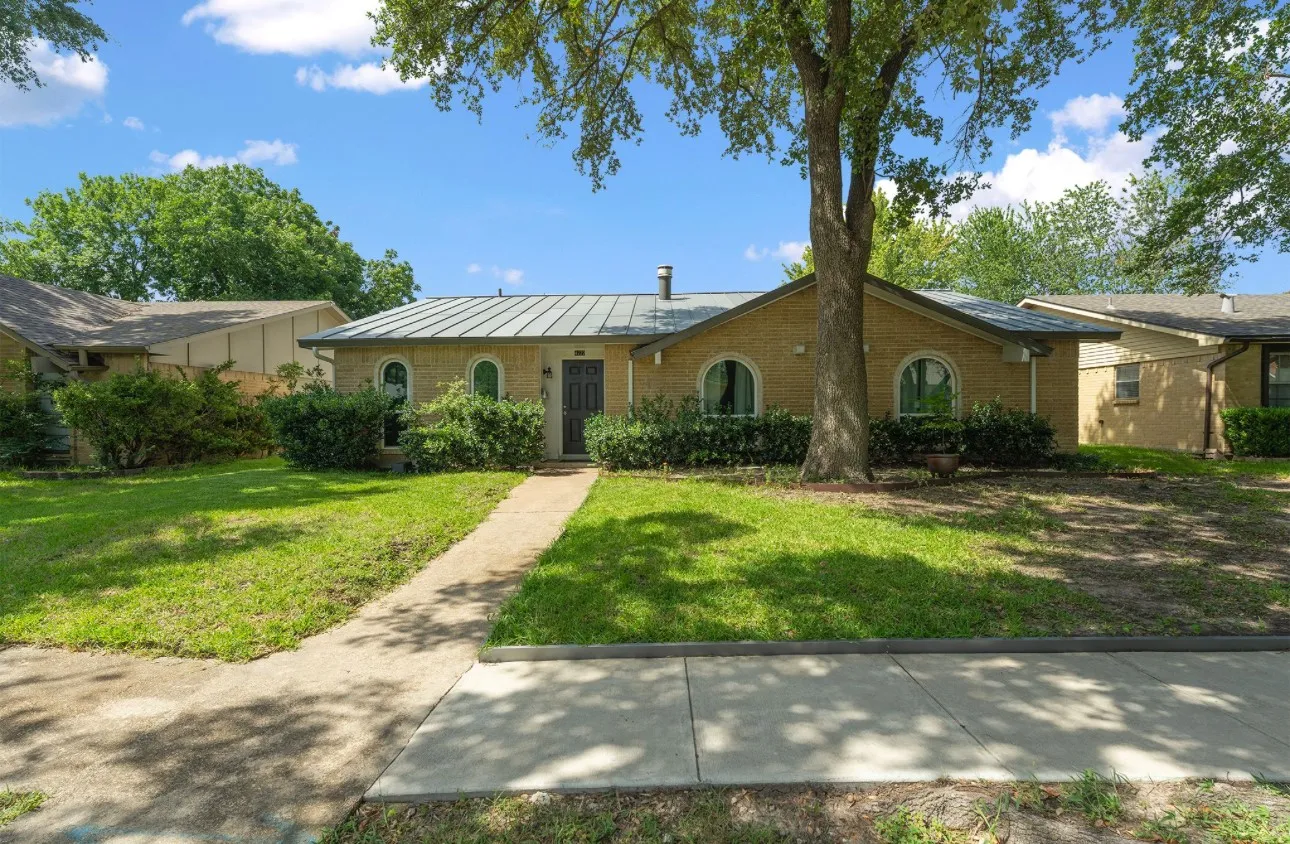 Brick exterior with arched window details, a metal roof, and a mature tree providing natural shade