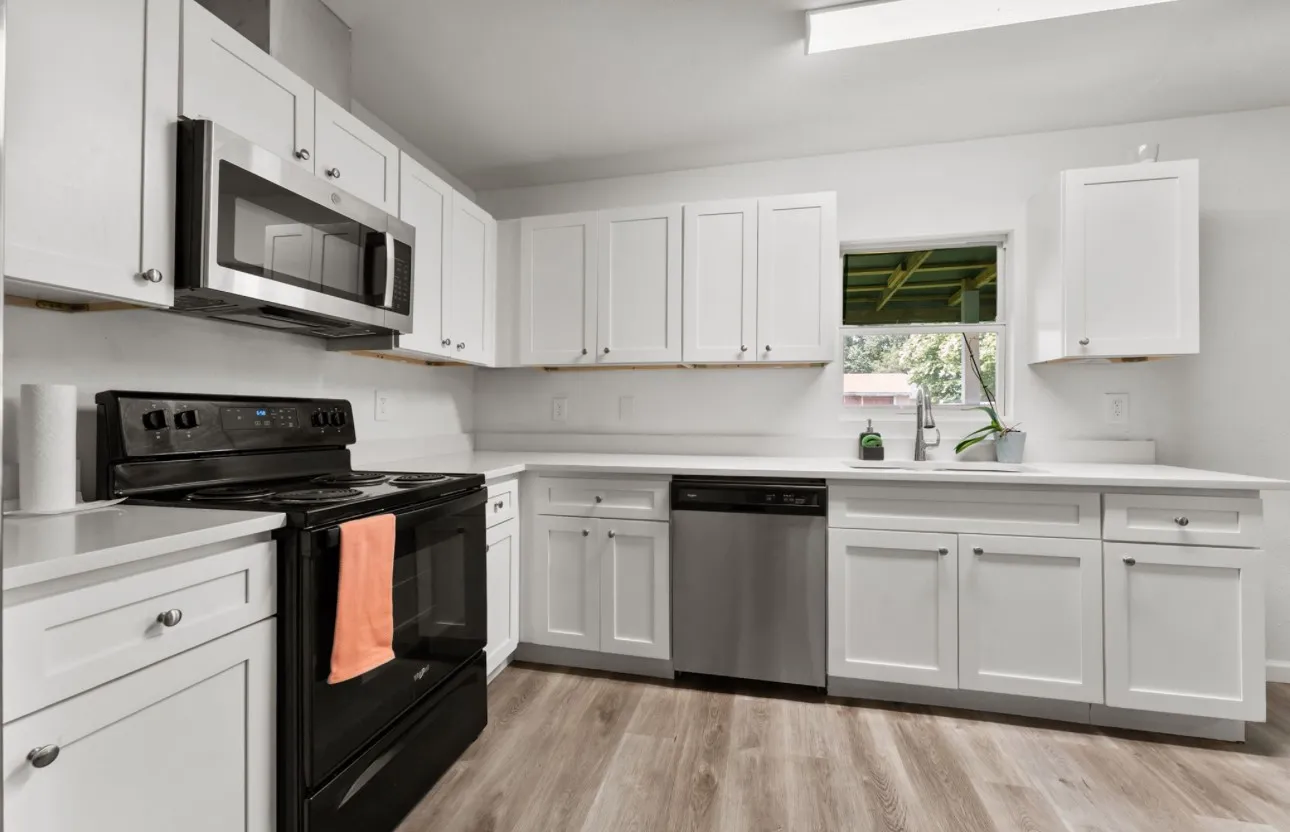 White shaker-style cabinetry, stainless steel microwave, black electric range, stainless steel dishwasher, and wood-finish flooring