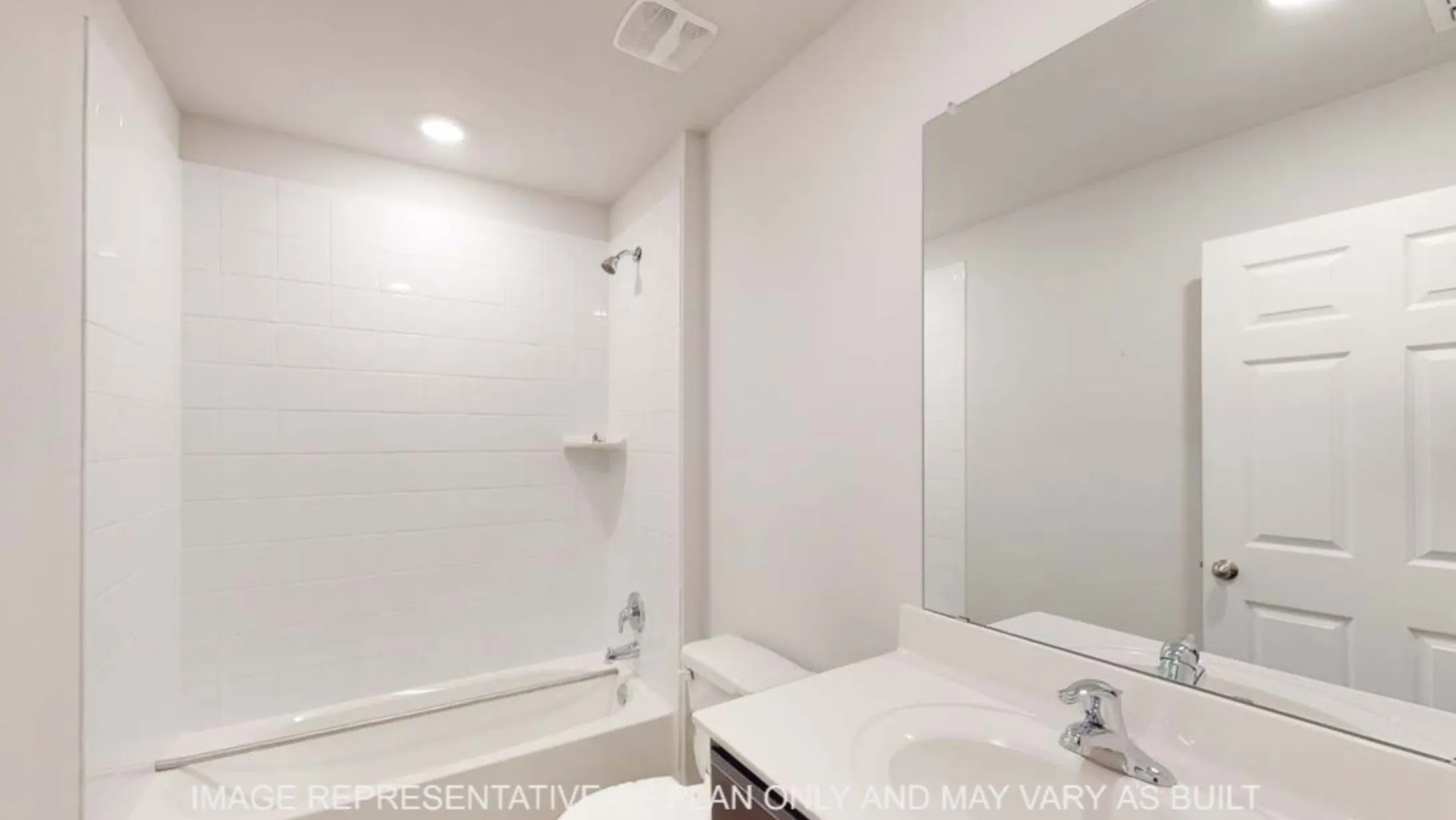 White subway tile shower surround with a built-in shelf, bathtub with chrome fixtures, single vanity with an integrated sink, and an expansive wall-mounted mirror