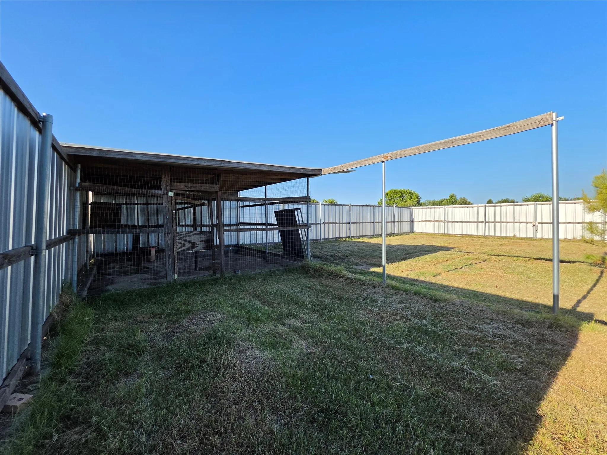 Enclosed structure with a wooden frame and metal siding, featuring an open-air extension with metal support poles