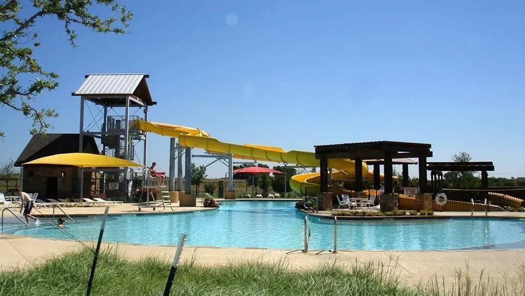 Expansive swimming pool area featuring a water slide, a multi-level structure with a metal roof, and shaded lounge areas under pergolas