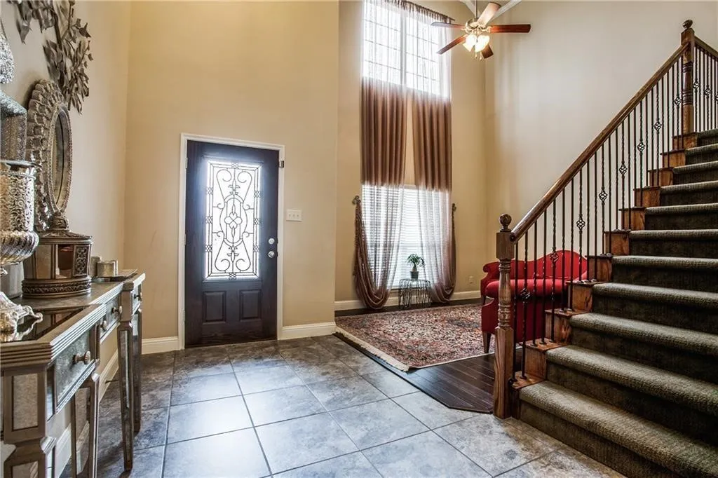 Entry foyer featuring tiled flooring, a dark wood entry door with decorative glass, a two-story ceiling, and a staircase with wrought iron balusters and wood handrail