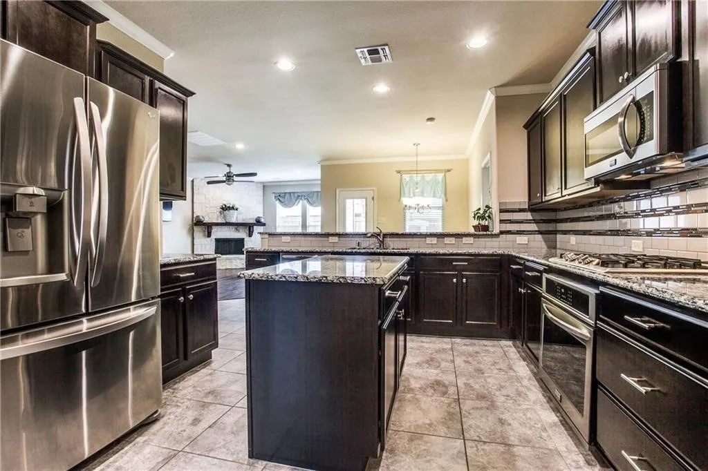 Built-in microwave, dark wood cabinetry, granite countertops, and tile flooring