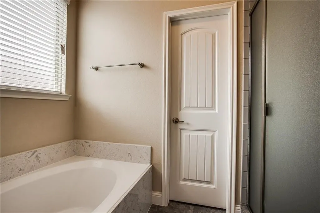 Built-in bathtub with a stone-finish surround, white paneled door, and frosted glass shower enclosure