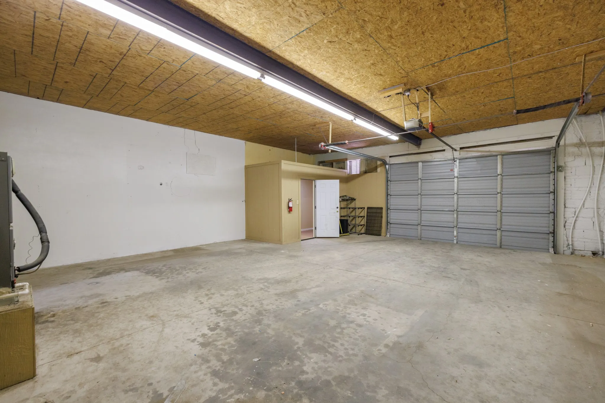 Concrete flooring, raw wood ceiling, fluorescent lighting, and roll-up garage door