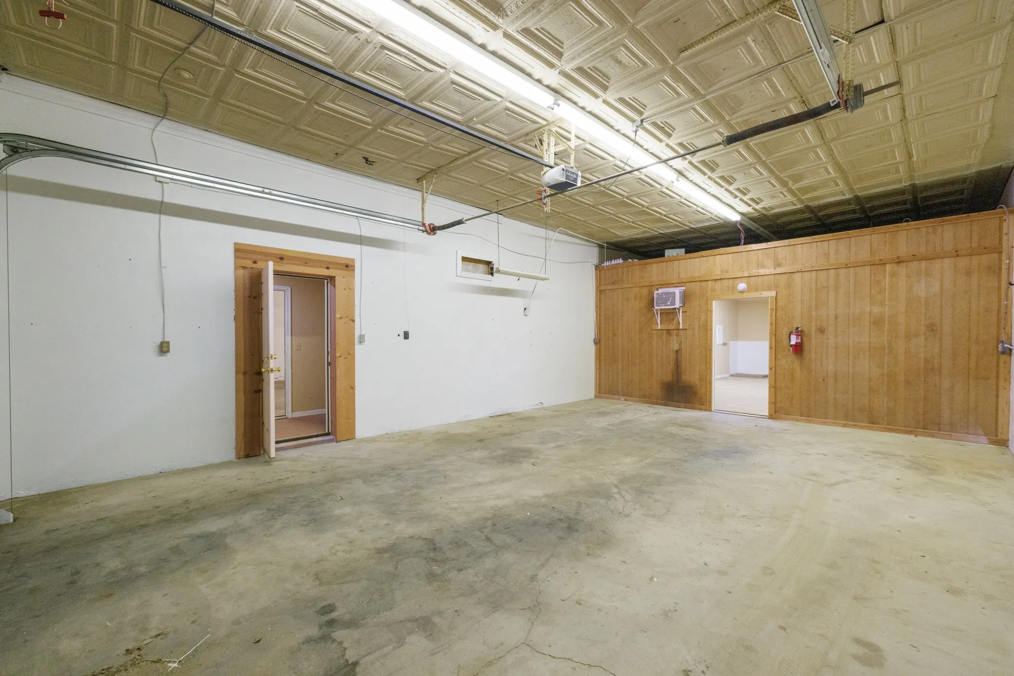 Concrete flooring, white walls, wood paneling, wood-frame doorways, and a patterned ceiling