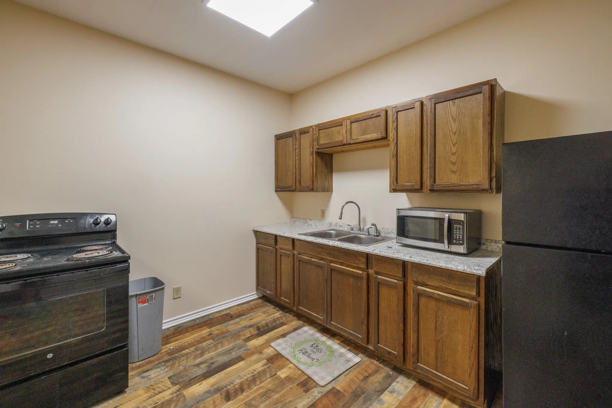 Kitchenette featuring wood-finish flooring, wood cabinetry, stone-look countertops, and a stainless steel sink