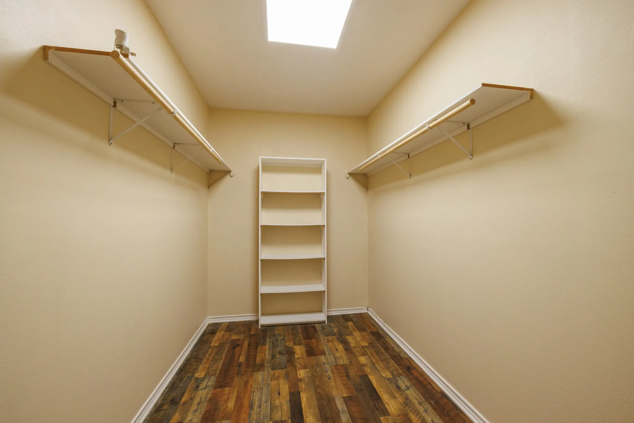 Walk-in closet featuring wood-finish flooring, built-in shelving, hanging rods, and an overhead light fixture