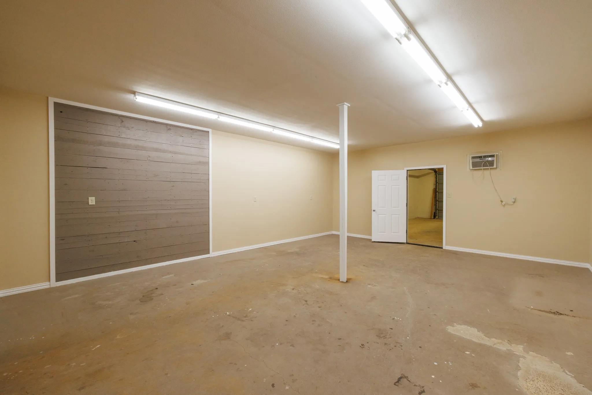Spacious room featuring a decorative wood-finish accent wall, multiple fluorescent ceiling lights, and concrete flooring