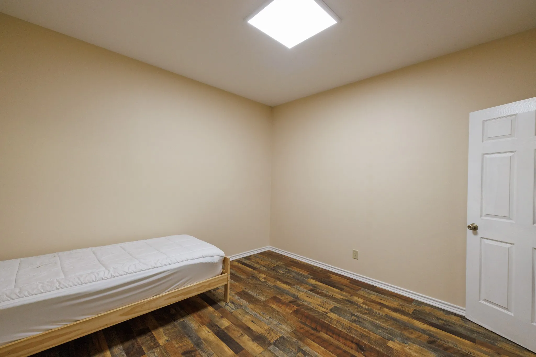 Recessed ceiling light, neutral wall tones, wood-finish flooring, white trim, paneled door