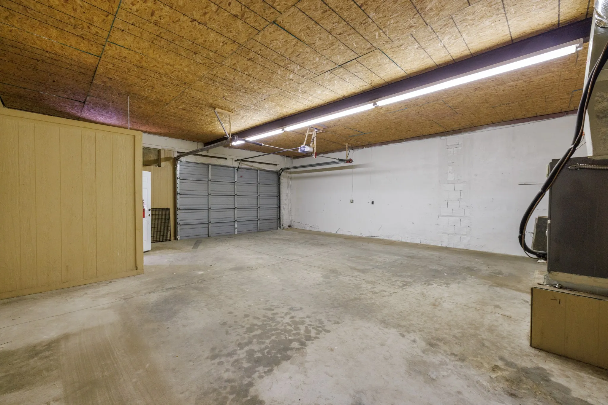 Concrete flooring, wood paneling, wood-finish ceiling, overhead fluorescent lighting, and a roll-up garage door