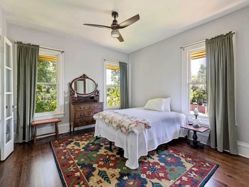 Bright bedroom with multiple French doors opening to natural light, wood-finish flooring, and ceiling fan
