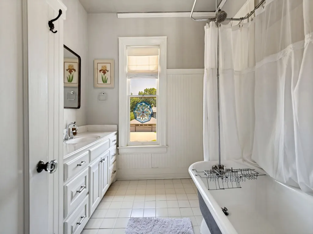 Charming hall bathroom featuring a white vanity with ample storage, ceramic tile flooring, and a classic pedestal soaking tub