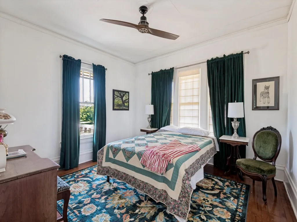Charming bedroom featuring hardwood flooring, ceiling fan, and abundant natural light from dual windows dressed in coordinating drapery