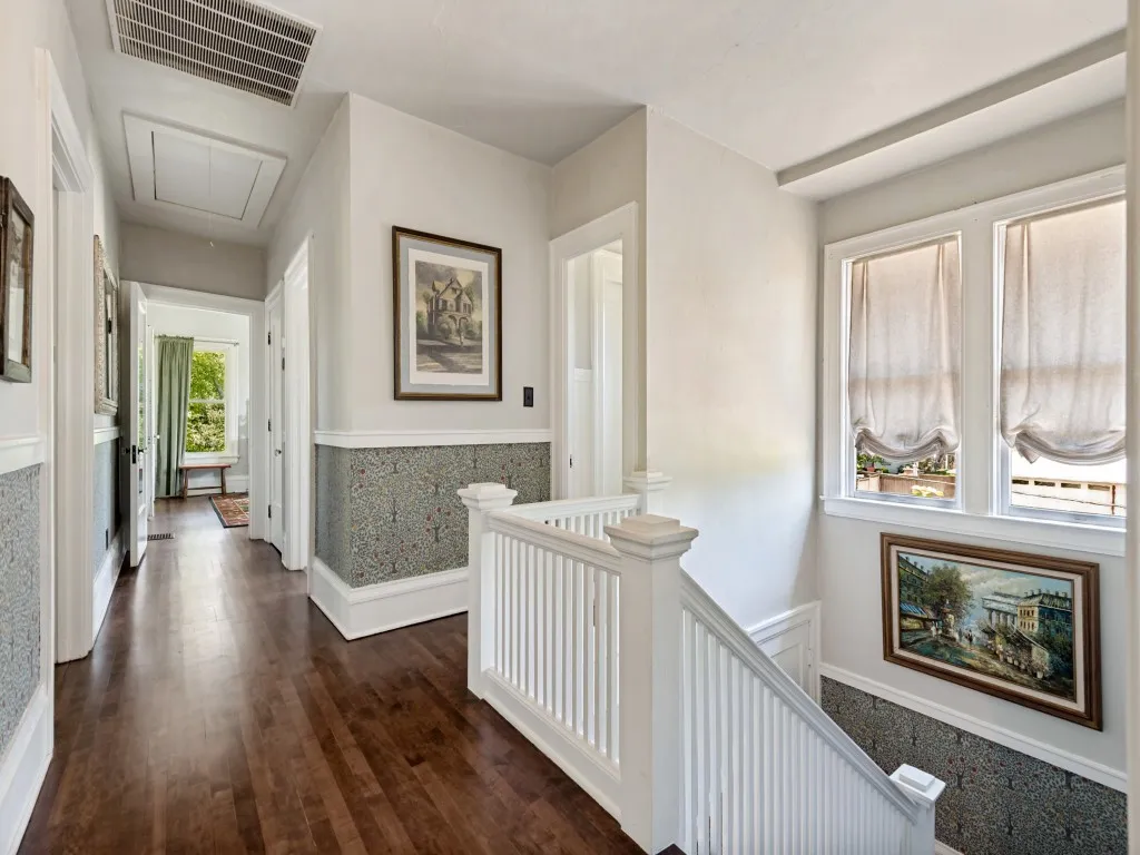 Upper-level hallway featuring rich wood-finish flooring, white painted millwork, and decorative wainscoting