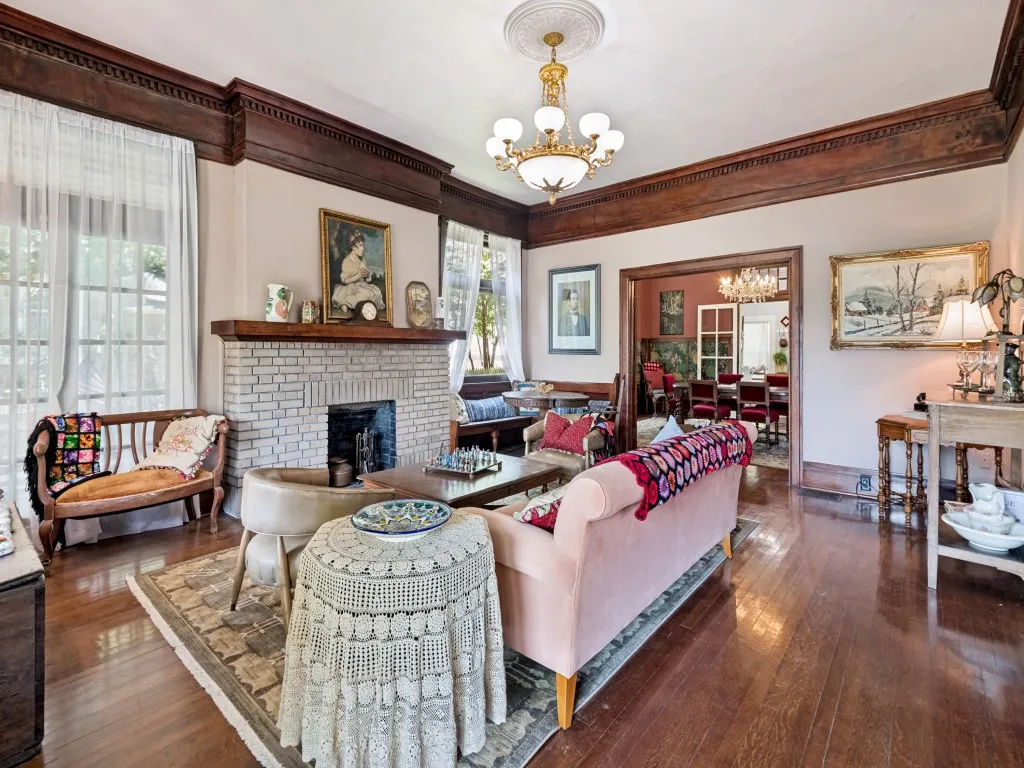 Elegant living room showcasing rich wood-beamed ceilings, original fireplace, and hardwood flooring throughout