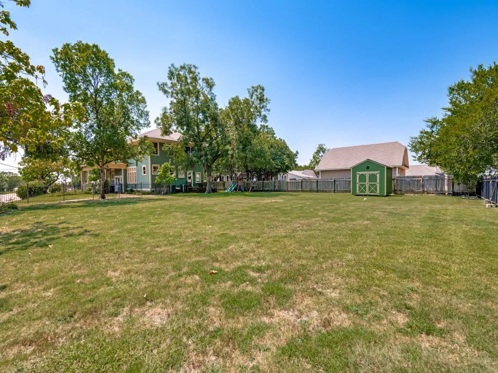 Expansive grass lawn featuring a detached storage shed, wood privacy fencing, and mature trees