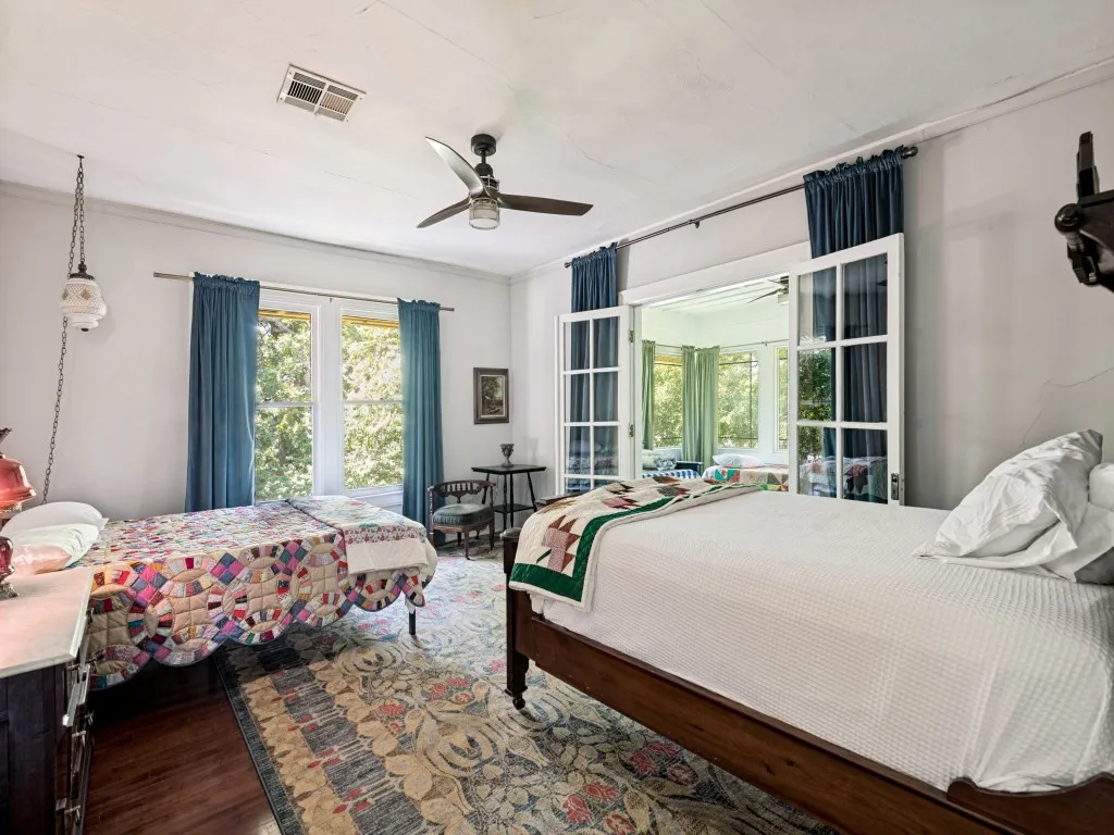 Spacious bedroom featuring hardwood flooring, ceiling fan, and abundant natural light from multiple windows dressed in blue drapery