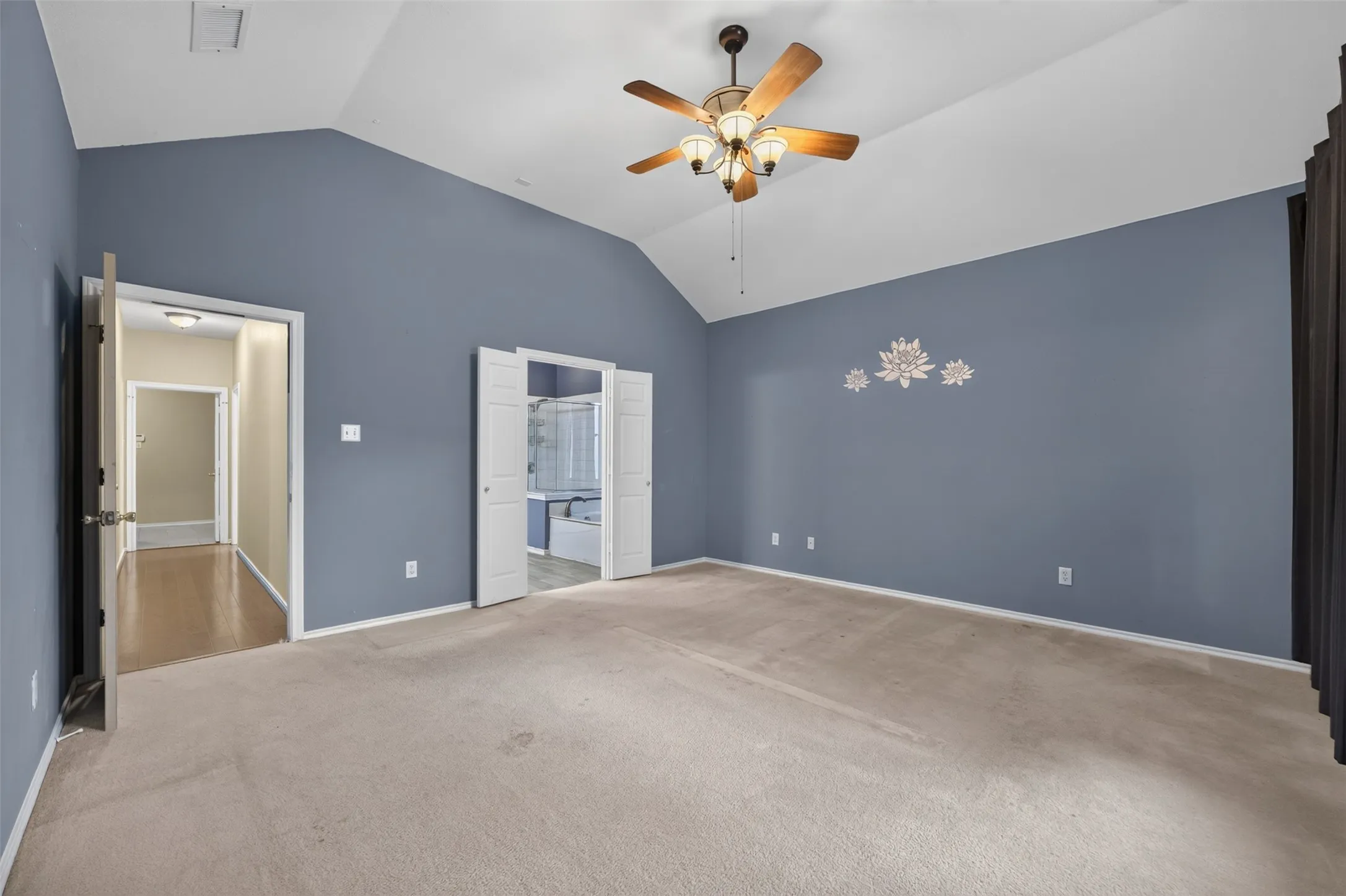 Vaulted ceiling, ceiling fan with integrated lighting, carpeted flooring, double bi-fold doors, and a decorative wall decal