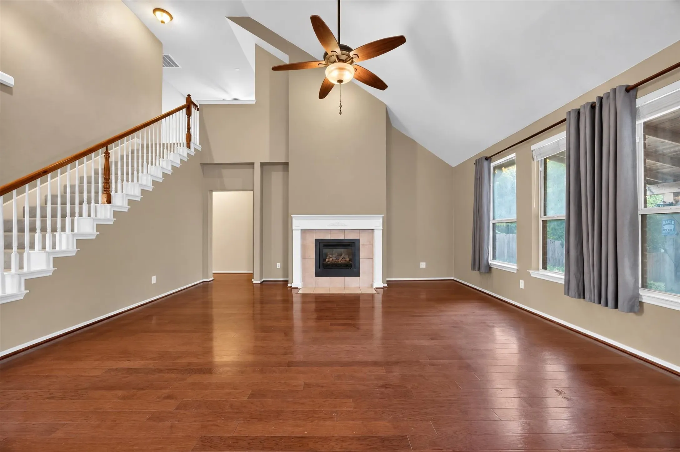 Vaulted ceilings, wood-finish flooring, staircase with wood handrail, fireplace with mantel, and multiple windows with drapery rods